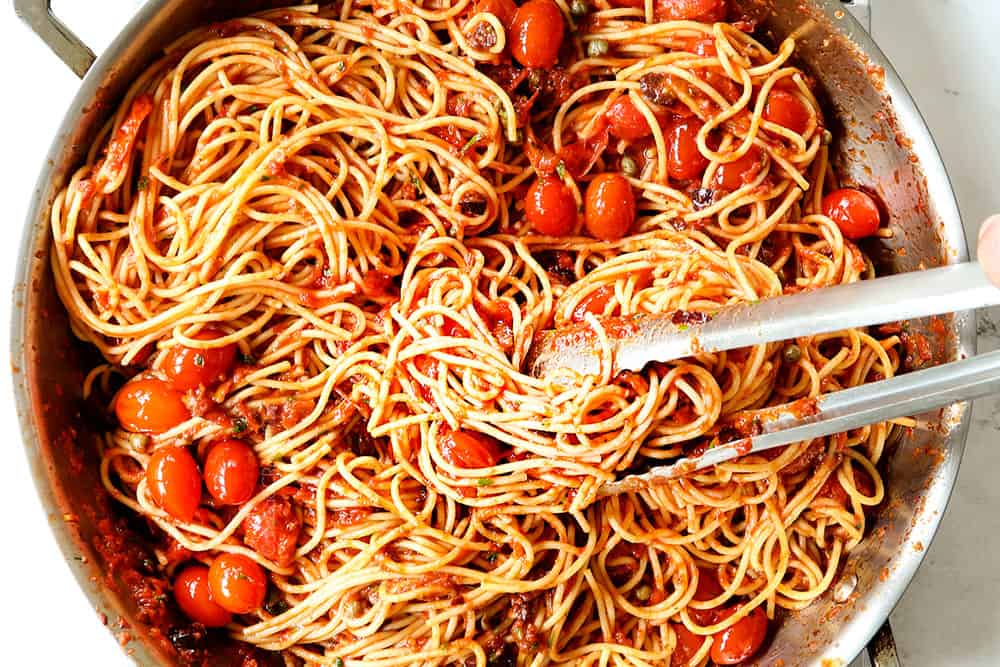 showing how to make Puttanesca recipe by stirring spaghetti into the Puttanesca sauce
