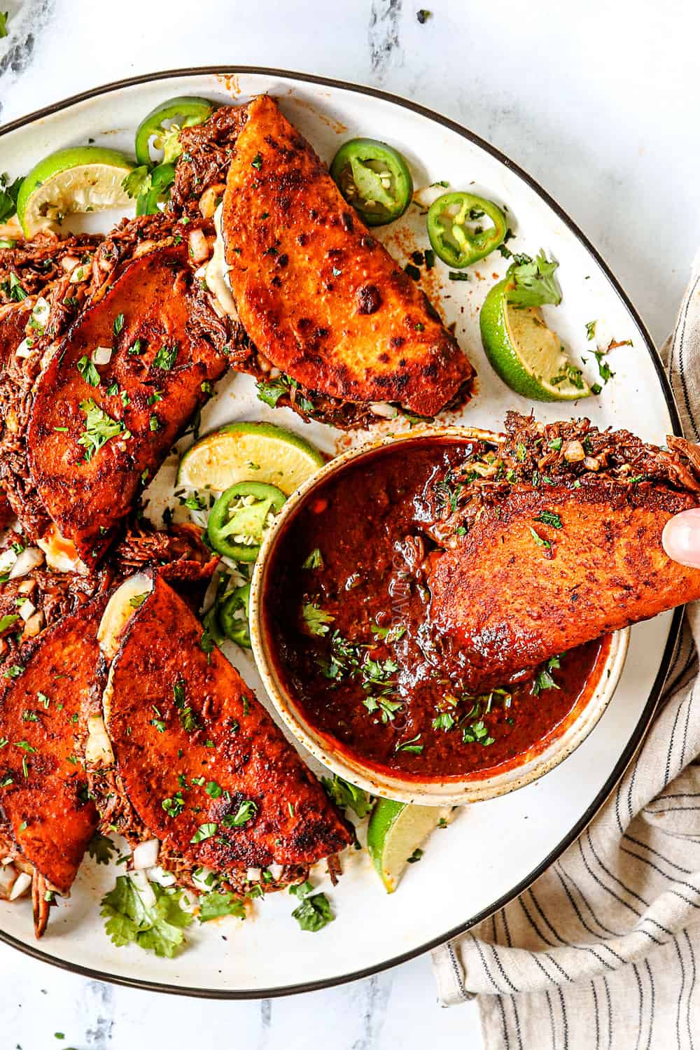 top view of quesa birria tacos on a plate with one being dipped in birria consomme