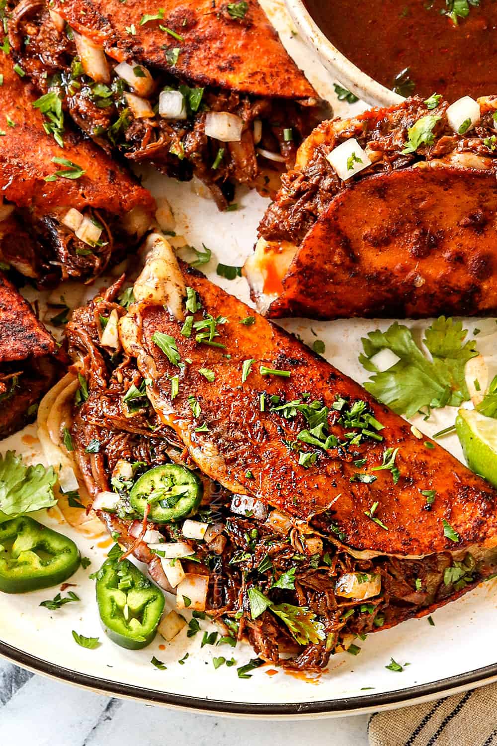 showing how to serve birria tacos by topping with chopped onions and cilantro