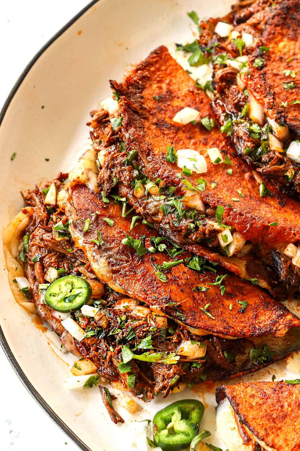 showing how to serve birria tacos by topping with chopped onions and cilantro