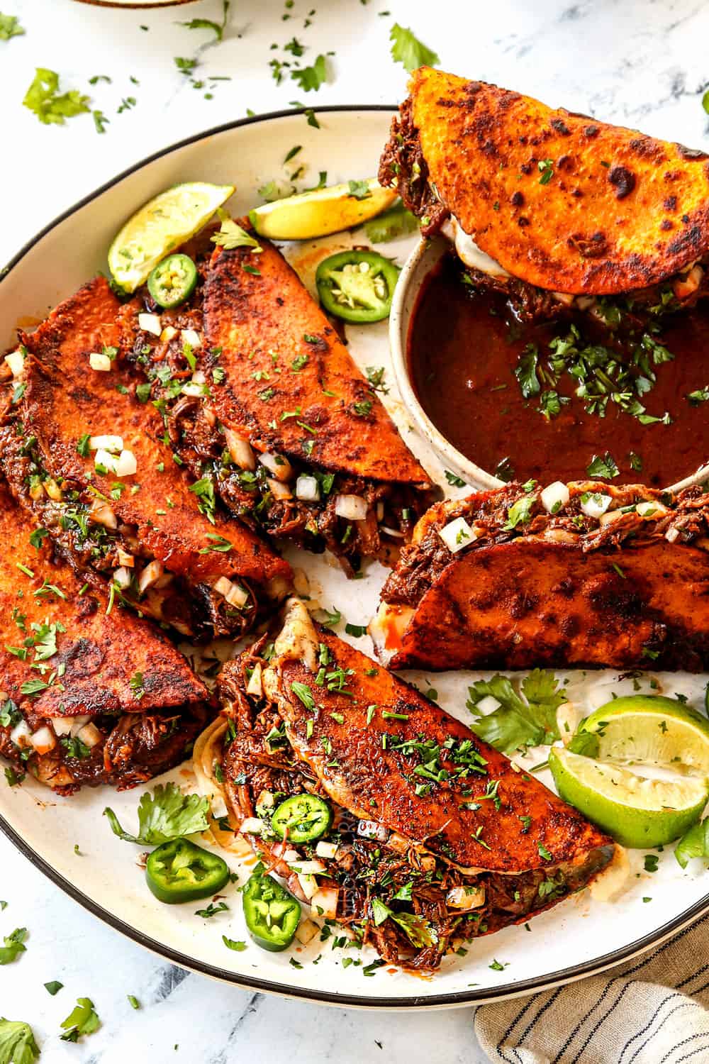 a plate of birria tacos garnished with cilantro and diced onions
