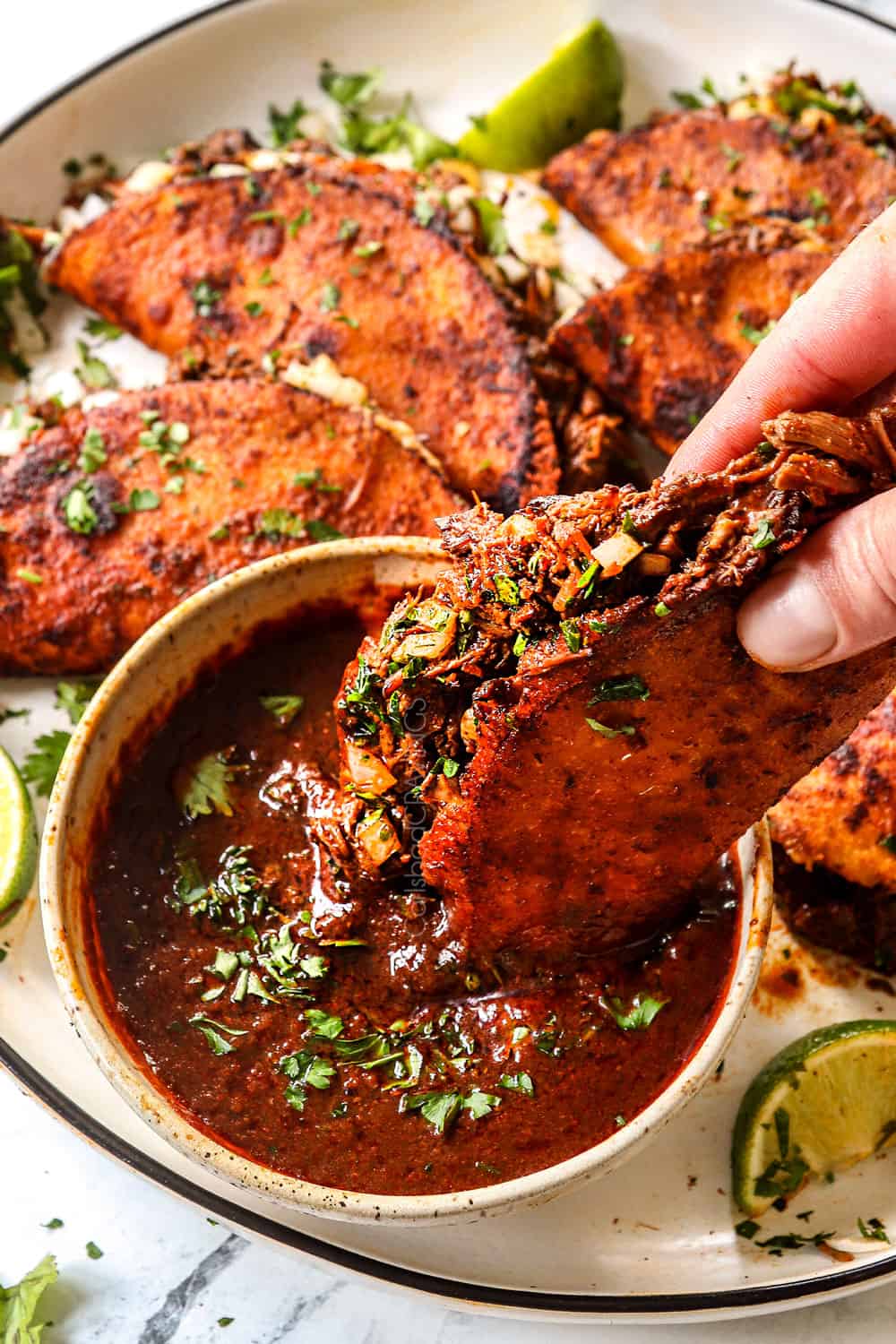 up close of dipping a birria taco into birria consome