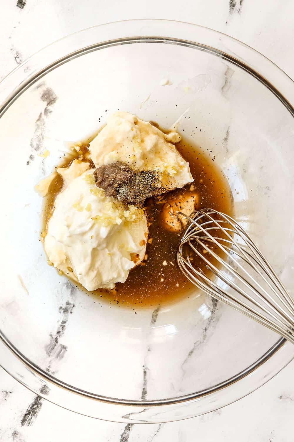 showing how to make Caesar Dressing by adding anchovies, Dijon, Worcestershire sauce, garlic, lemon juice and mayonnaise to a glass bowl
