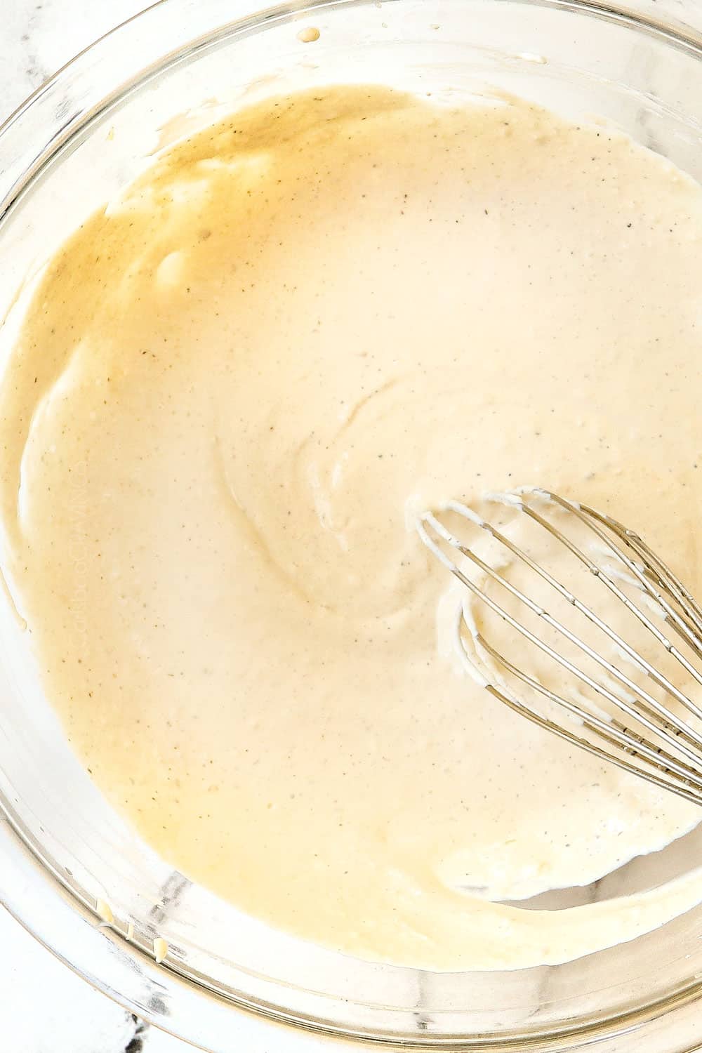 showing how to make Caesar Dressing by whisking all of the ingredients together in a glass bowl until smooth