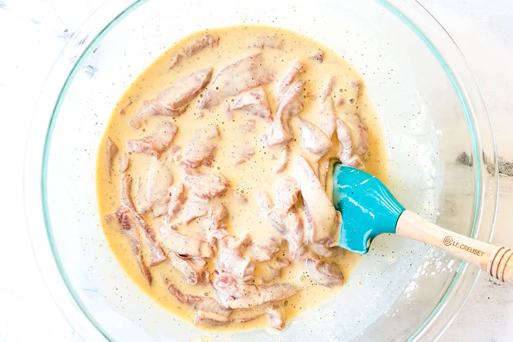showing how to make ginger beef recipe ty tossing the beef in batter in a glass bowl