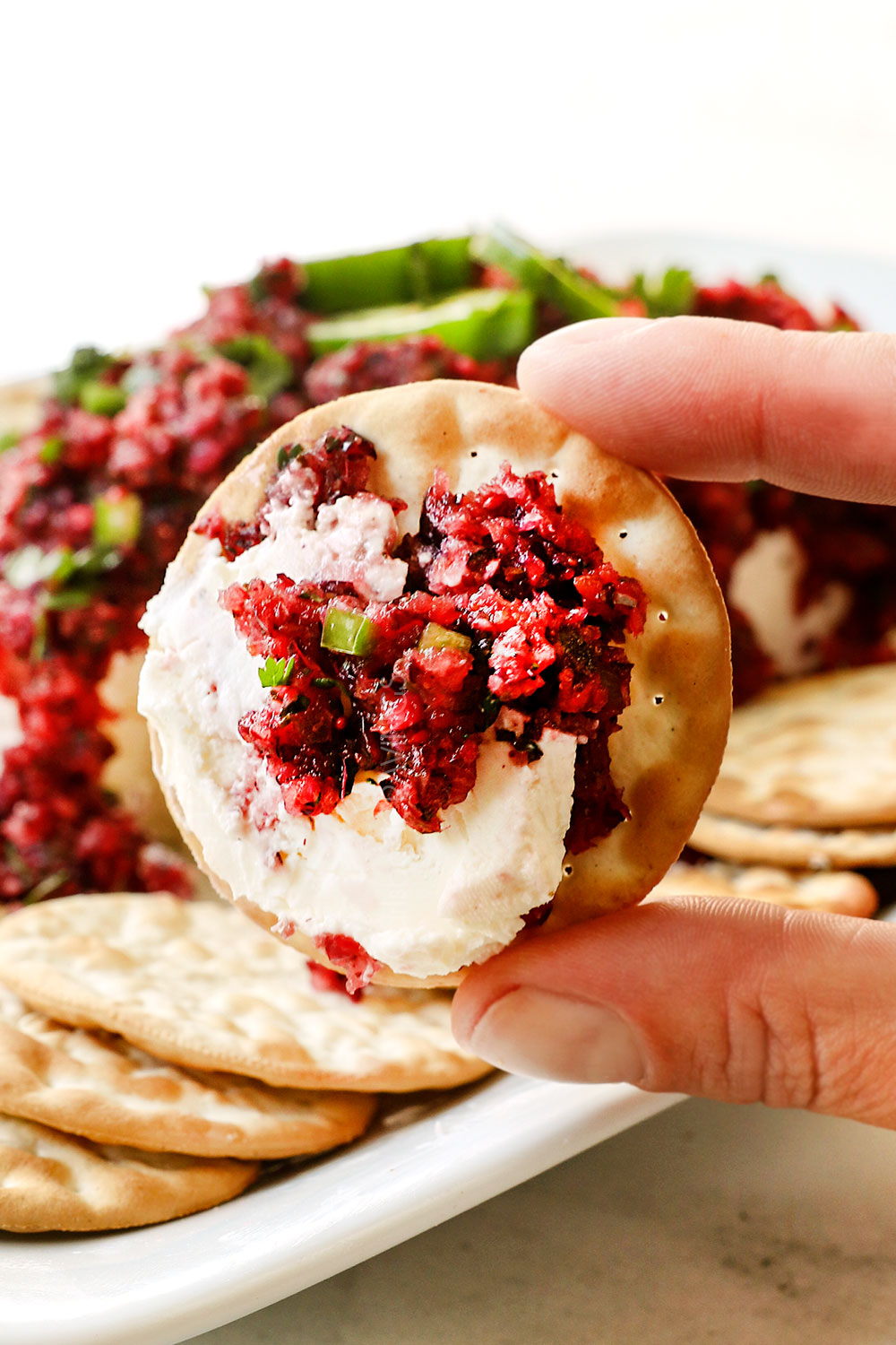showing how to serve cranberry salsa with up close of holding a cracker with cream cheese and cranberry salsa