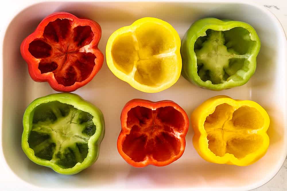 showing how to make stuffed peppers by lining bell peppers with their tops cut off in a baking dish with a little water