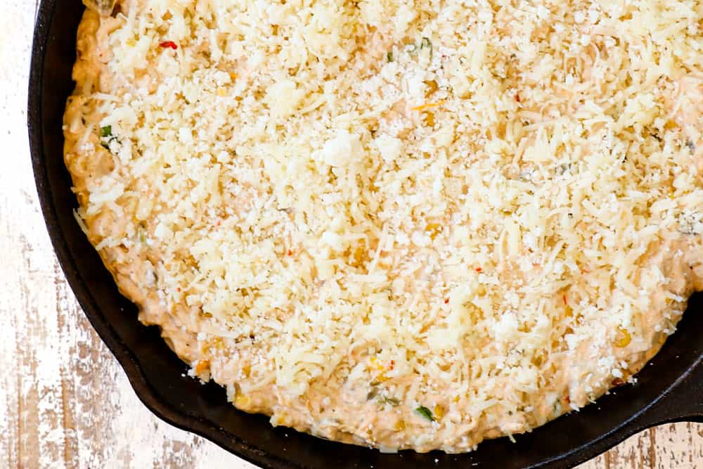 showing how to make corn dip recipe by adding dip to a cast iron skillet then adding pepper Jack cheese on top