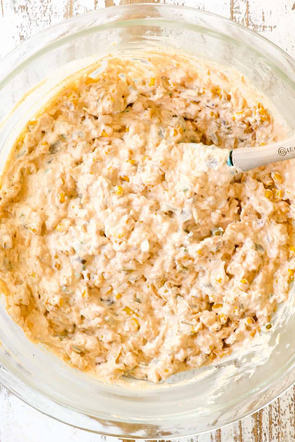 showing how to make corn dip by stirring cream cheese, sour cream and corn together in a glass mixing bowl