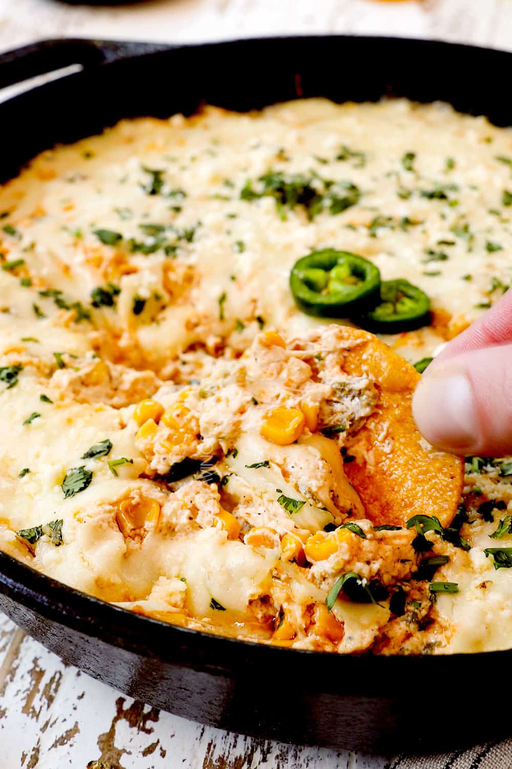 up close of scooping up hot corn dip recipe with corn, jalapenos and cilantro