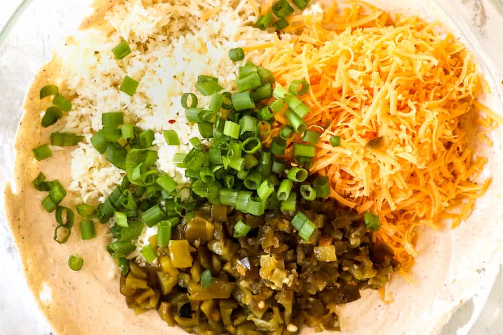showing how to make Mexican corn dip recipe by adding cheese, green onions, green chilies, jalapenos and cotija to the mixing bowl