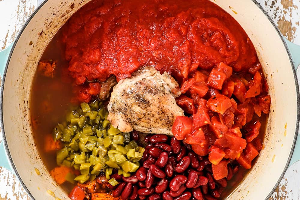showing how to make healthy chicken chili recipe by adding chicken, beans, tomatoes, and bell peppers to a Dutch oven