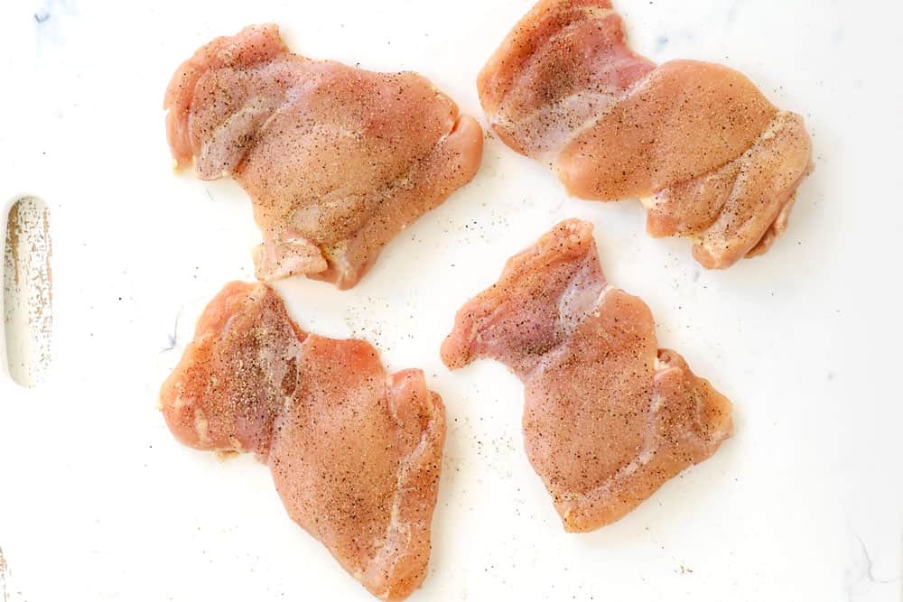 showing how to make creamy chicken noodle soup recipe by seasoning chicken thighs with salt and pepper on a white cutting board