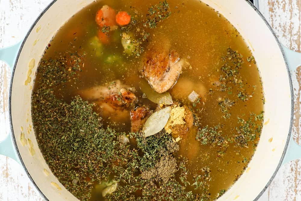 showing how to make creamy chicken noodle soup recipe by adding seared chicken, chicken broth, Italian seasonings and bay leaf to Dutch oven