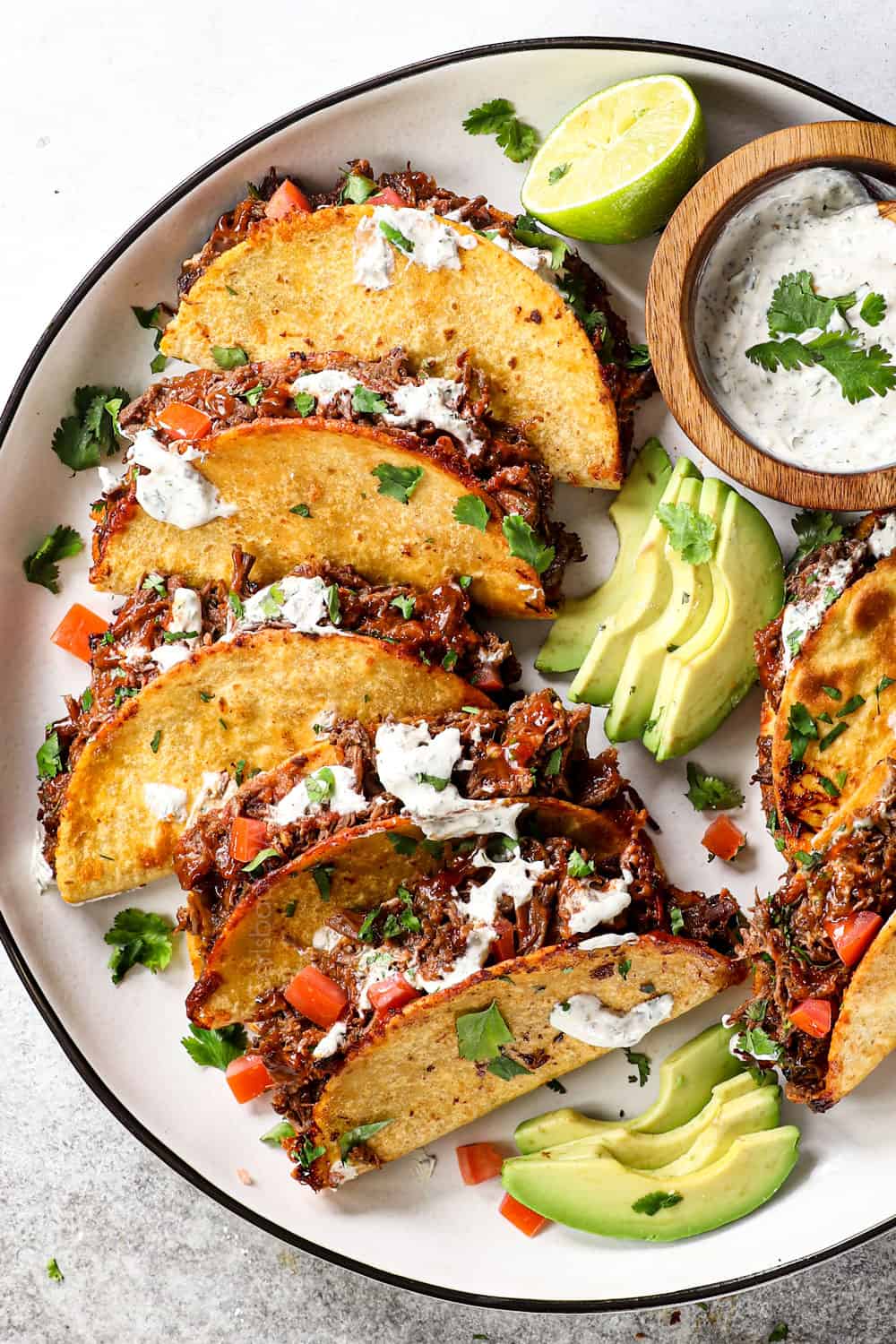 top view of shredded beef tacos lined on a plate with tomatoes