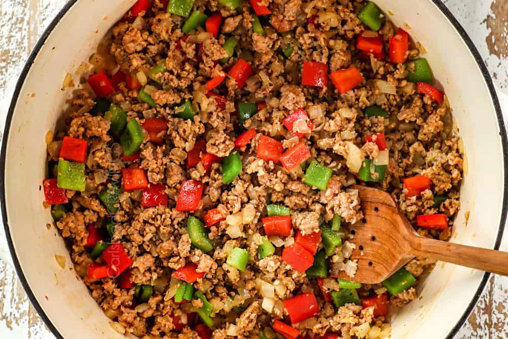 showing how to make stuffed pepper soup recipe by browning Italian sausage, onions, garlic and bell peppers together in a large Dutch oven