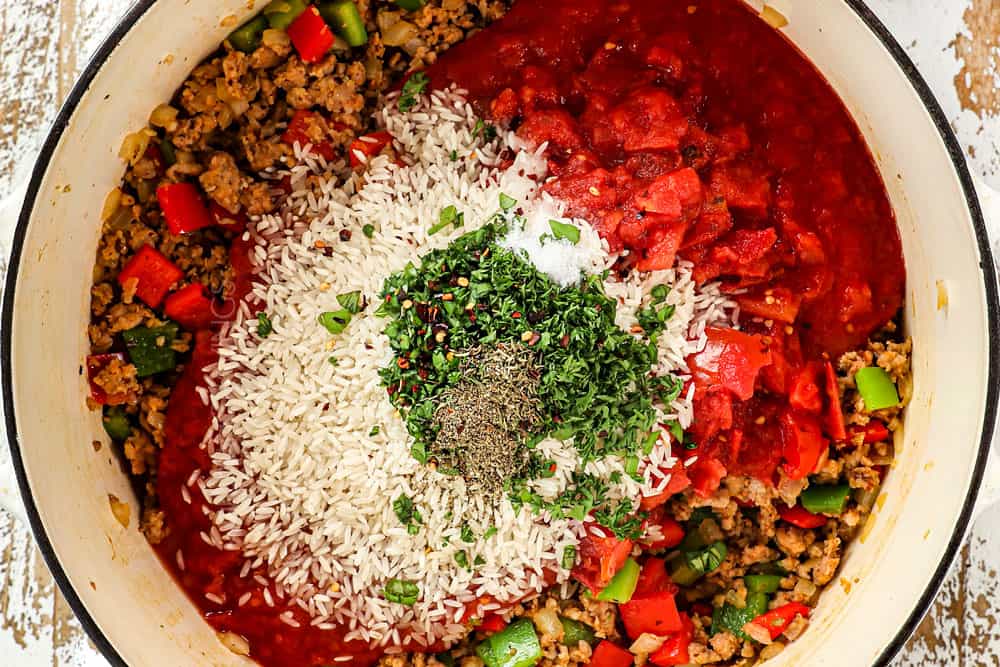 Showing how to make Stuffed Bell Pepper Soup recipe by adding crushed tomatoes, diced tomatoes, rice, basil, parsley, oregano and beef broth to the sausage and bell peppers in a soup pot