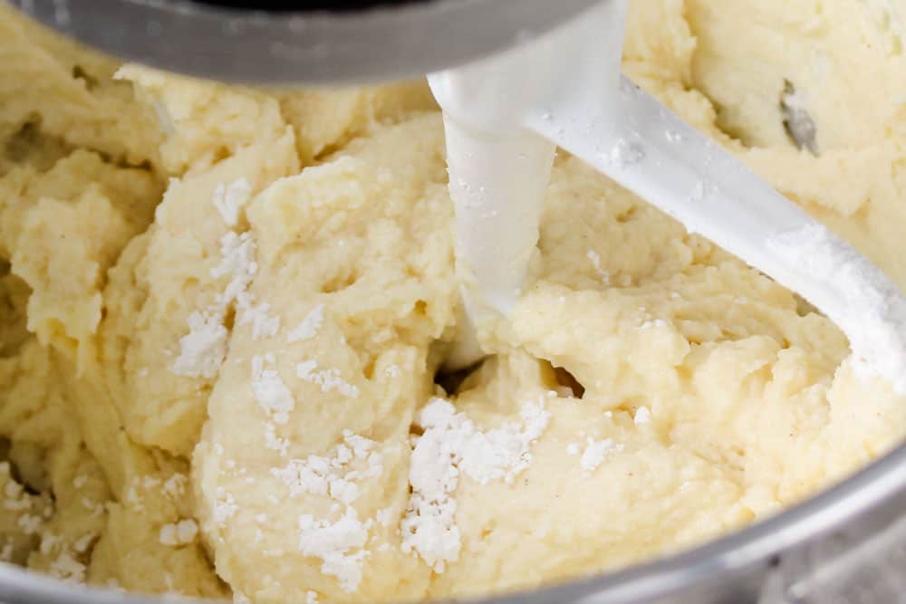 showing how to make cannoli dip recipe by beating in vanilla extract, almond extract and powdered sugar until smooth and creamy
