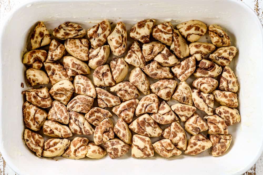 showing how to make cinnamon roll casserole recipe by adding sliced Pillsbury cinnamon rolls to a 9x13 dish