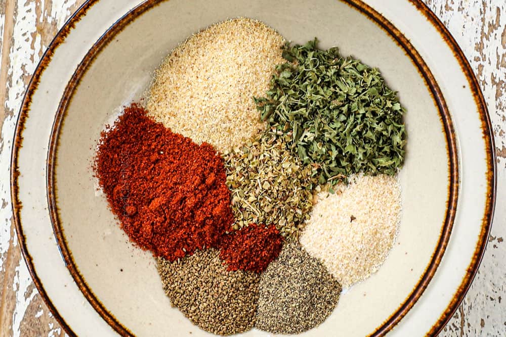 showing how to make fish sticks by mixing seasonings together in a bowl: garlic powder, onion powder, paprika, pepper, parsley and oregano