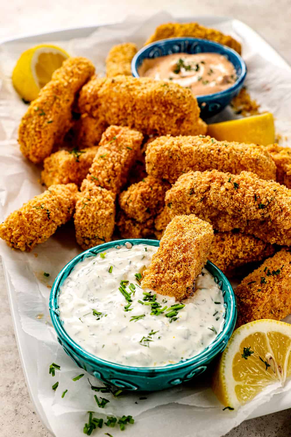 air fryer fish sticks on a platter with a fishstick dunked in tartar sauce