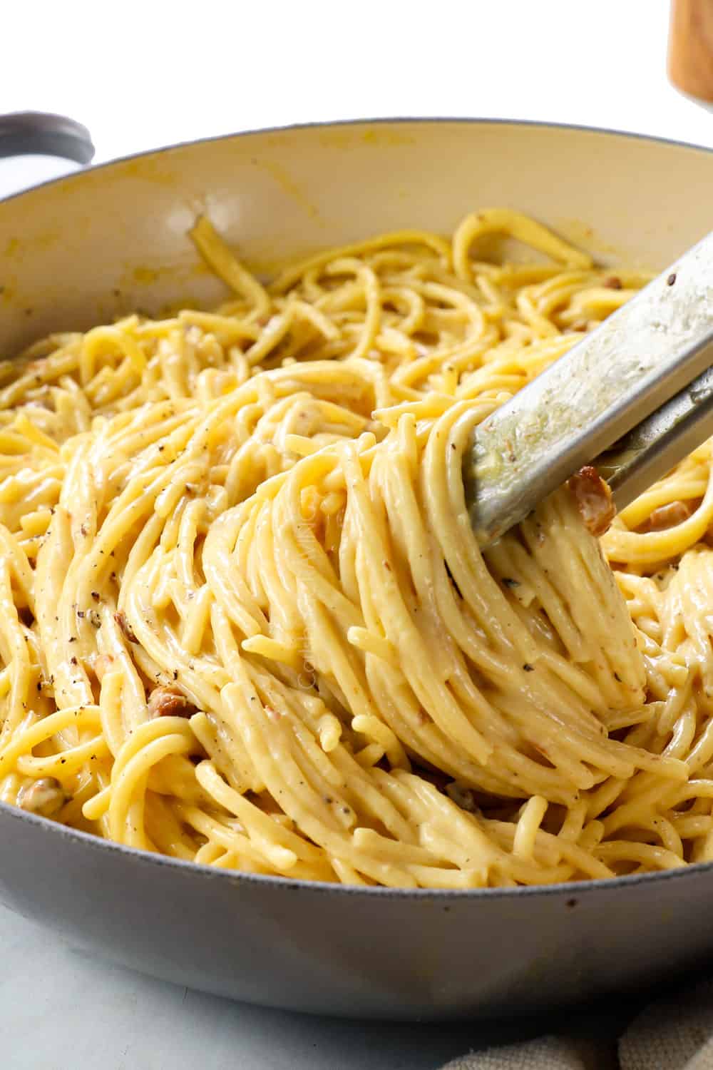 showing how to make carbonara recipe by tossing pasta with egg sauce showing how creamy it is
