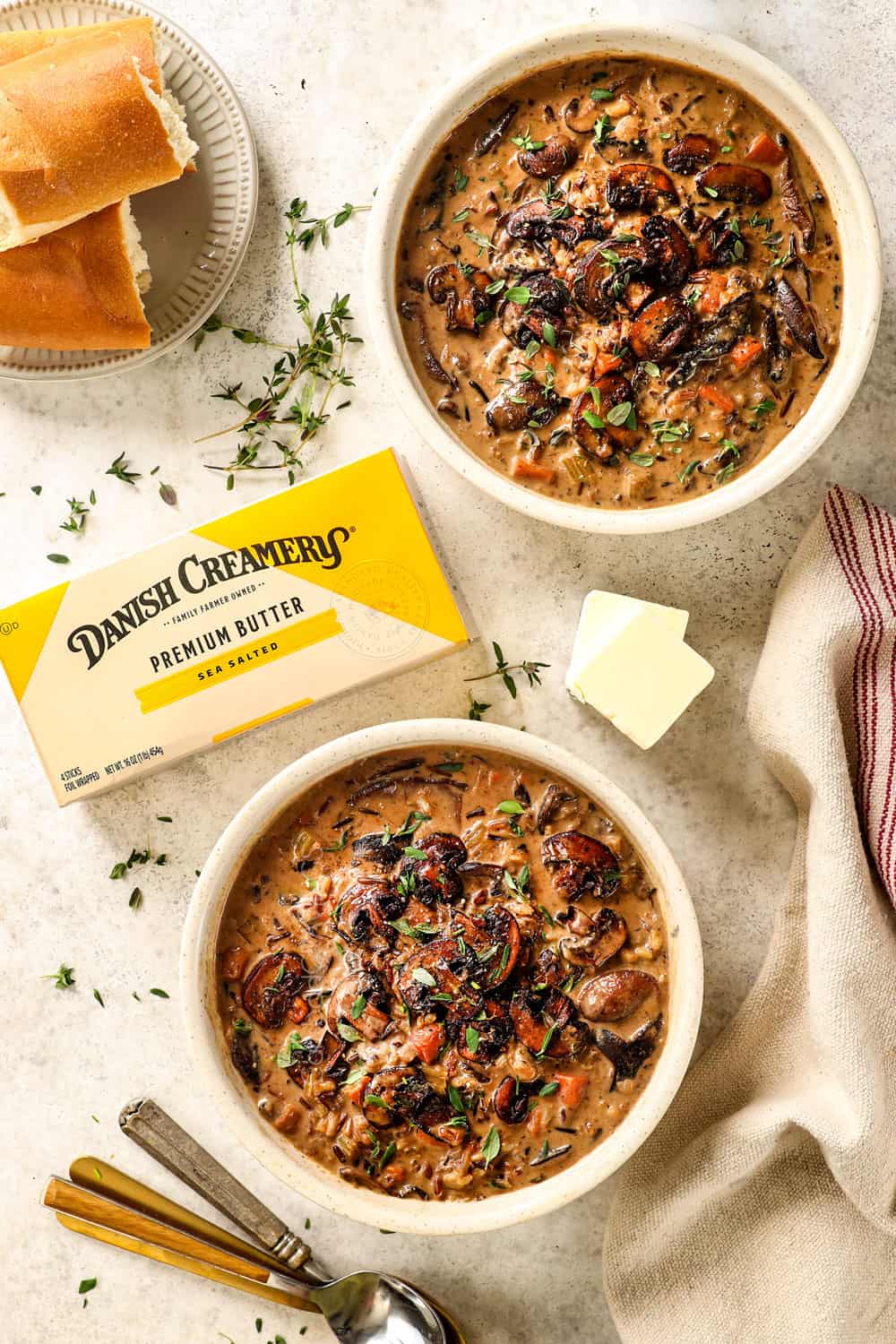 top view of two bowls of creamy mushroom soup garnished by fresh thyme with bread, showing how to serve the soup