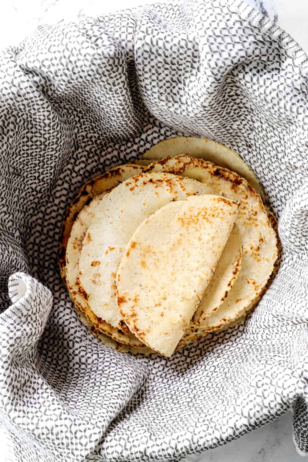 showing how to make corn tortilla recipe by keeping a stack of tortillas warm in wrapped in a damp kitchen towel