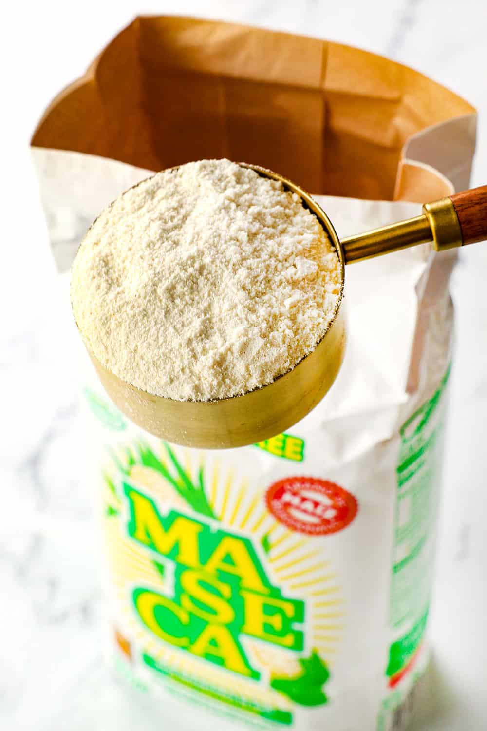 showing how to make corn tortillas with masa harina by scooping masa harina in a measuring cup