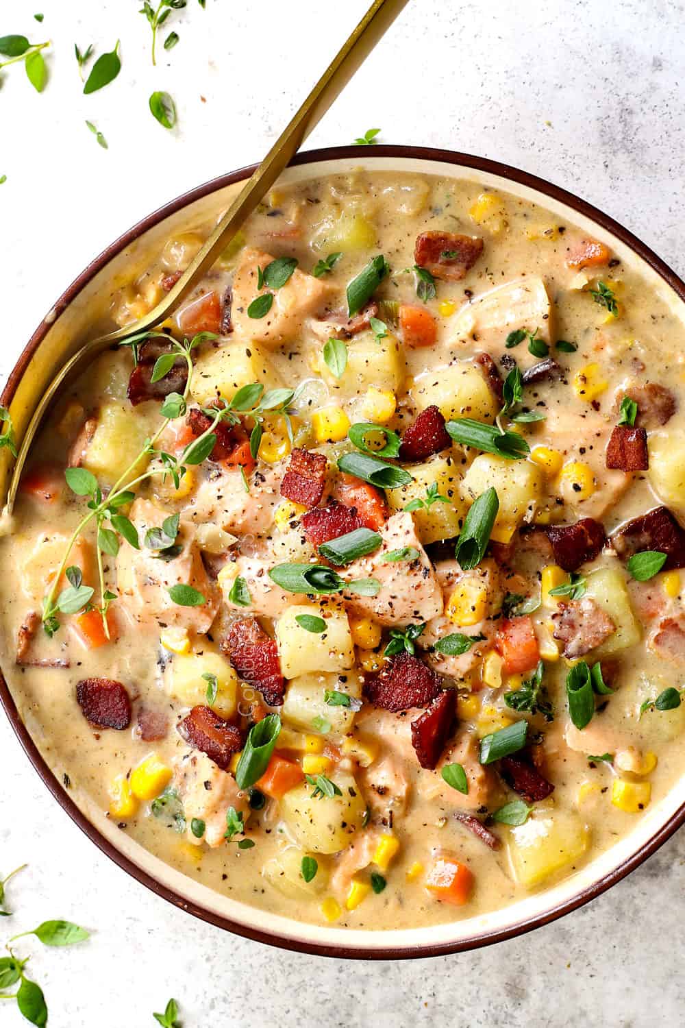 top view of fish chowder with salmon, bacon, corn and potatoes in a bowl garnished with fresh thyme and green onions