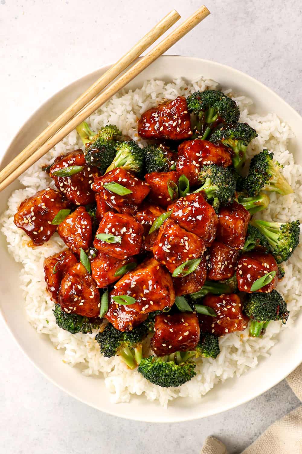 top view of honey sesame chicken over rice in a bowl garnished with green onions and sesame seeds