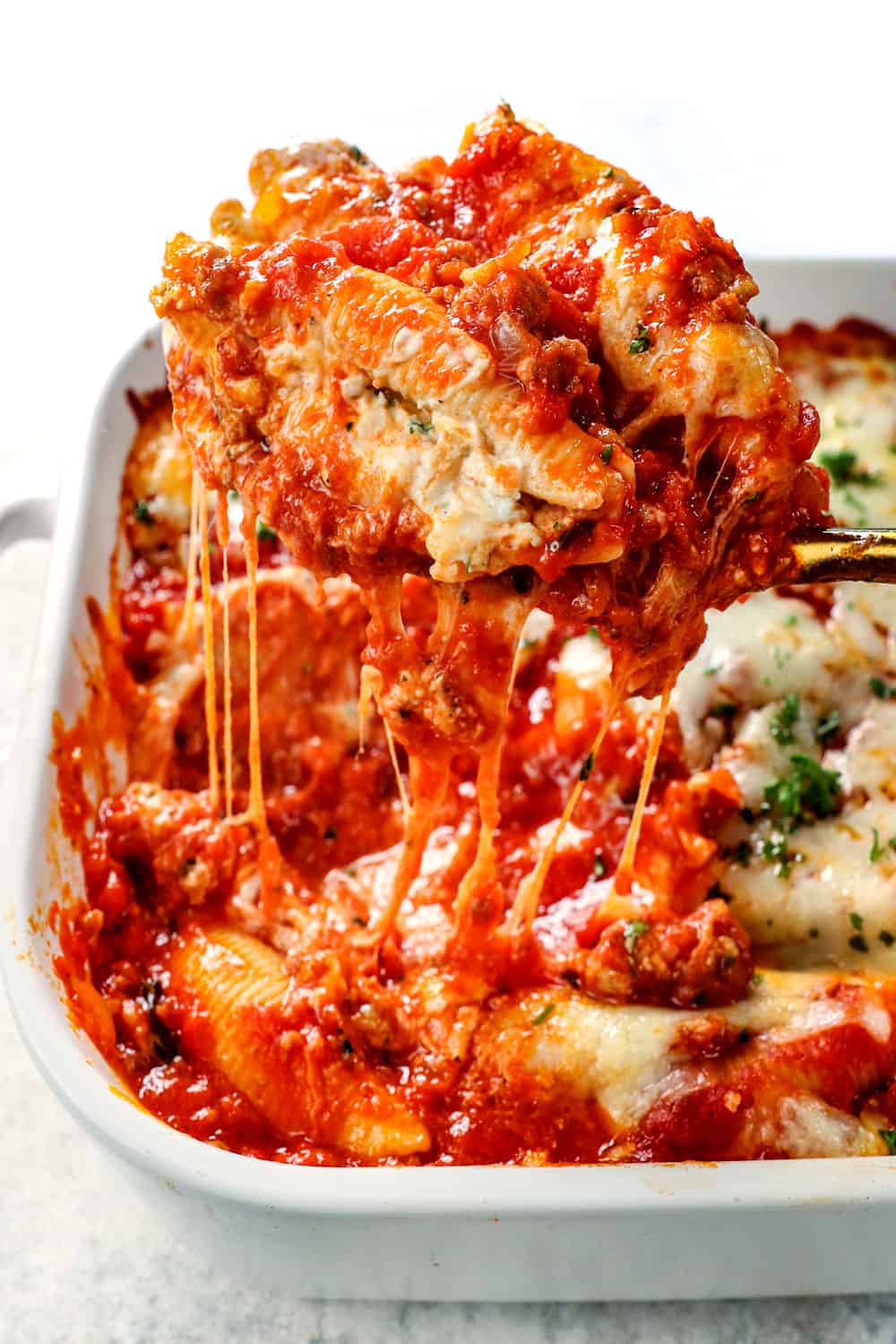 picking up a scoop of stuffed shell recipe showing how cheesy and meaty it is