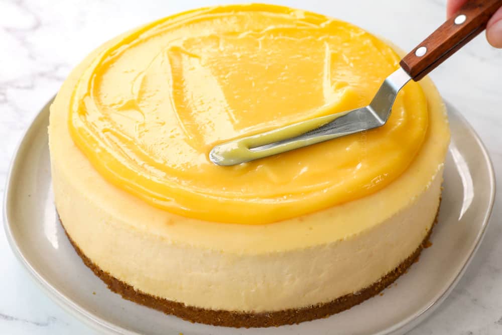 showing how to make lemon cheesecake recipe by spreading cheesecake with lemon curd