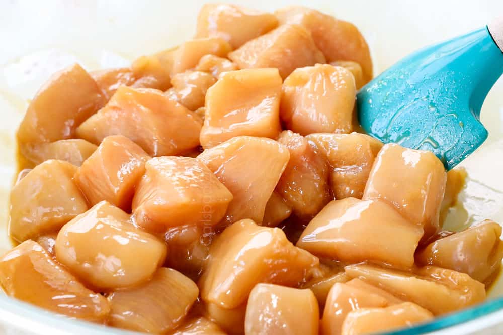 showing how to make cashew chicken stir fry by marinating chicken breast chunks in a bowl with soy sauce, rice wine, sesame oil, cornstarch