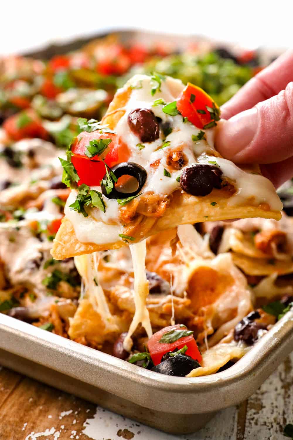 showing how cheesy the shredded chicken nachos are by picking up a tortilla chip with stringy cheese