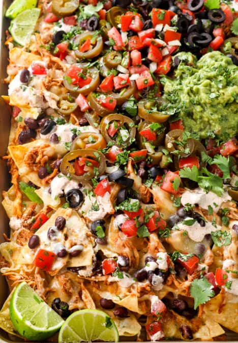 chicken nachos baked in the oven with shredded chicken, cheese and beans then topped with guacamole, sour cream, pico de gallo, olives and jalapenos