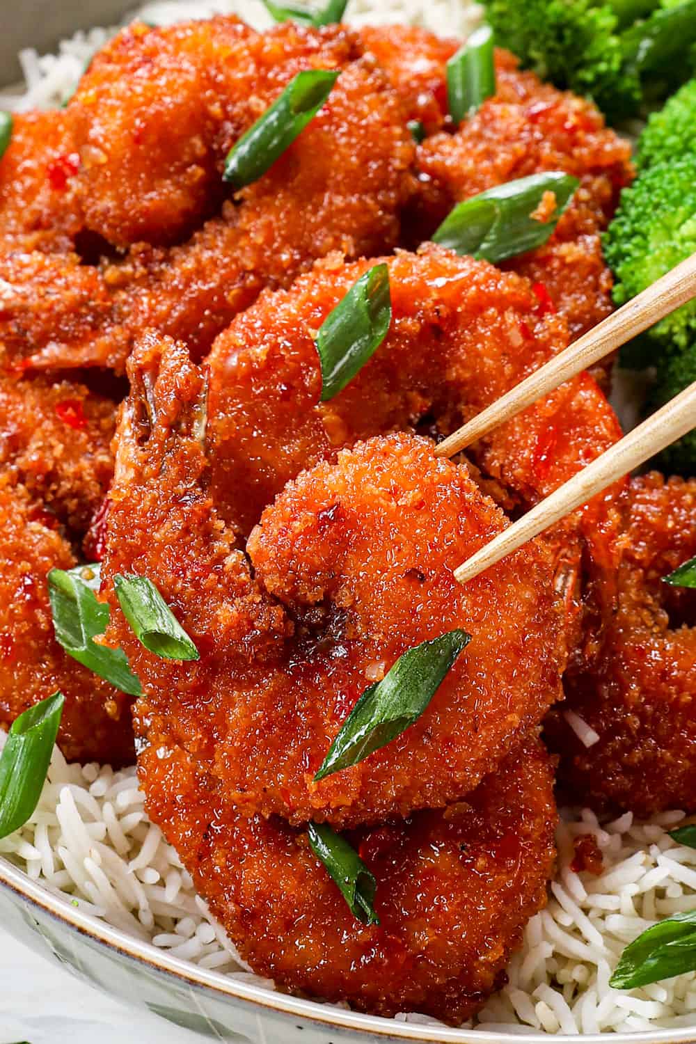 showing how to serve crispy firecracker shrimp by adding to a bowl of rice with stir fried broccoli and picking shrimp up with chopsticks