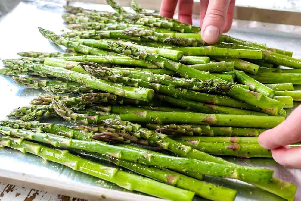 showing how to make lemon pepper salmon recipe by tossing asparagus with olive oil, salt and lemon pepper seasoning