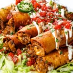 up close of taquitos with beef and cheese, topped with pic de gallo, sour cream and guacamole