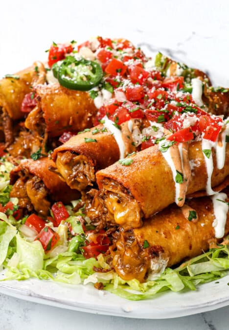 up close of taquitos with beef and cheese, topped with pic de gallo, sour cream and guacamole