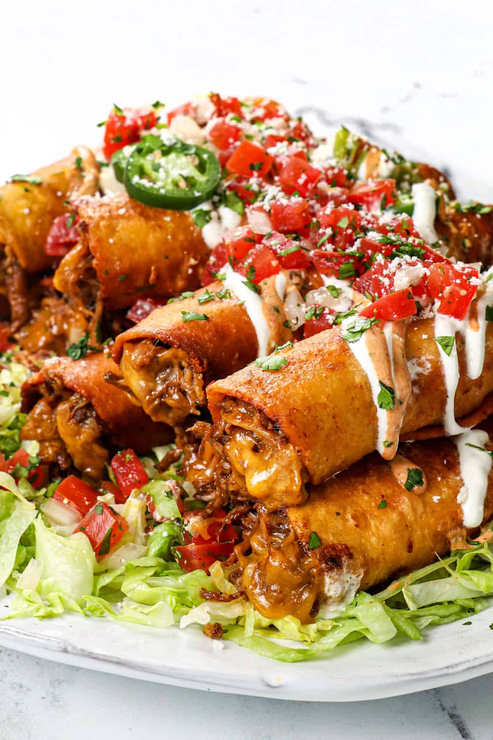up close of taquitos with beef and cheese, topped with pic de gallo, sour cream and guacamole