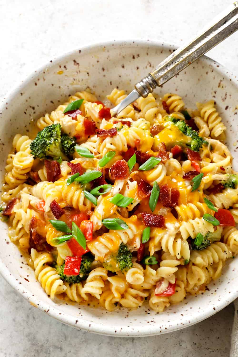 top view of chicken bacon ranch casserole with pasta being served in a bowl garnished by bacon