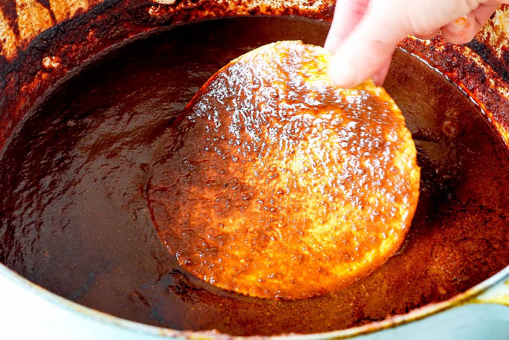 showing how to make chicken birria tacos recipe by dipping the tortilla in the consume