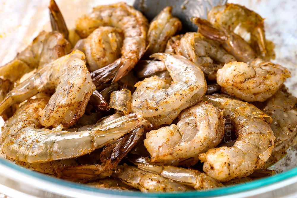 showing how to make garlic creamy Tuscan Shrimp by seasoning shrimp in a bowl with salt, pepper, onion powder, garlic powder and paprika