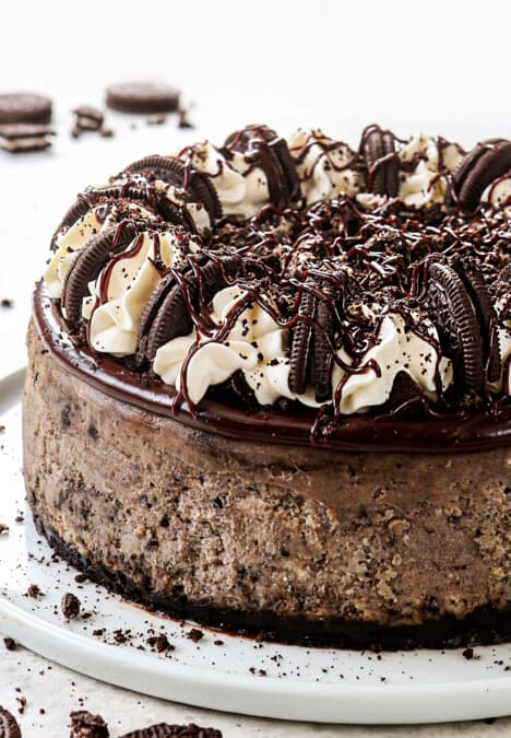 side view of Oreo cheesecake recipe showing how to decorate it with whipped cream, crushed Oreos and chocolate drizzle