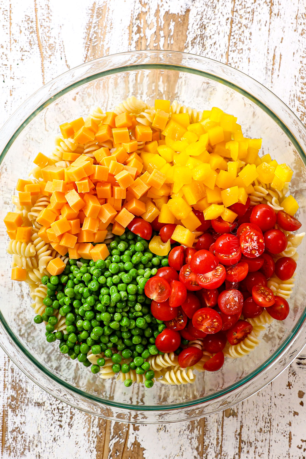 top view showing ingredients for pasta bacon ranch salad: pasta, tomatoes, peas, bell peppers, cheese and homemade ranch dressing
