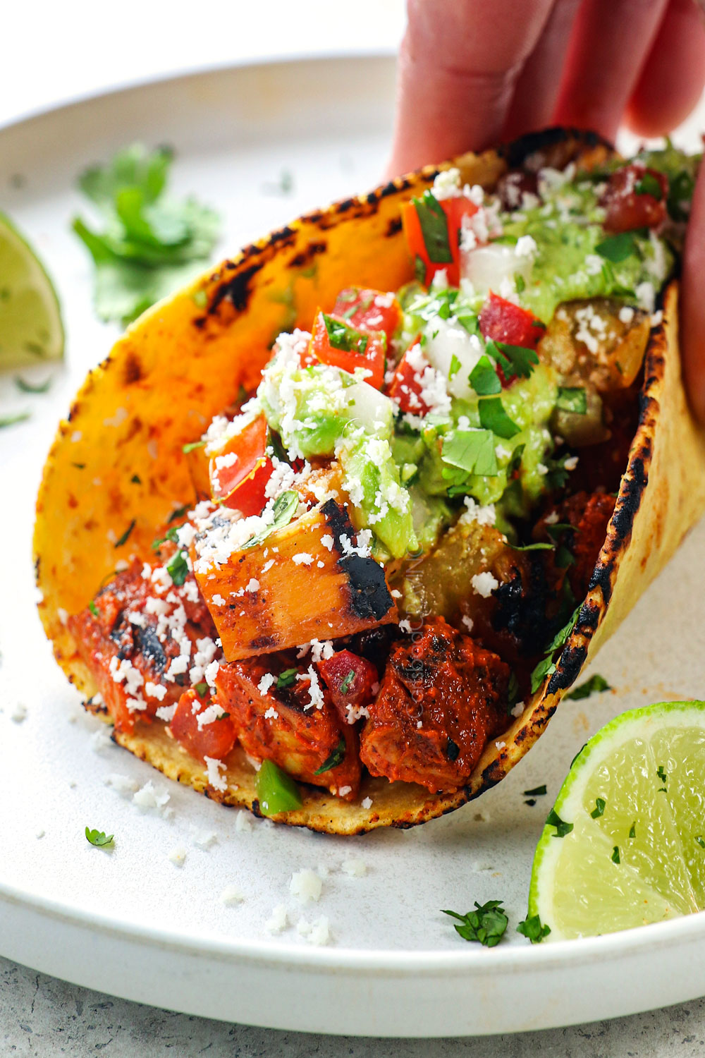 a hand holding Chicken Al Pastor Taco with guacamole and pico de gallo