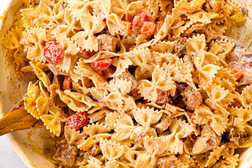 showing how to make Chicken Caesar Pasta Salad by adding half of the dressing to the pasta and chicken and tossing to combine and then chilling the salad