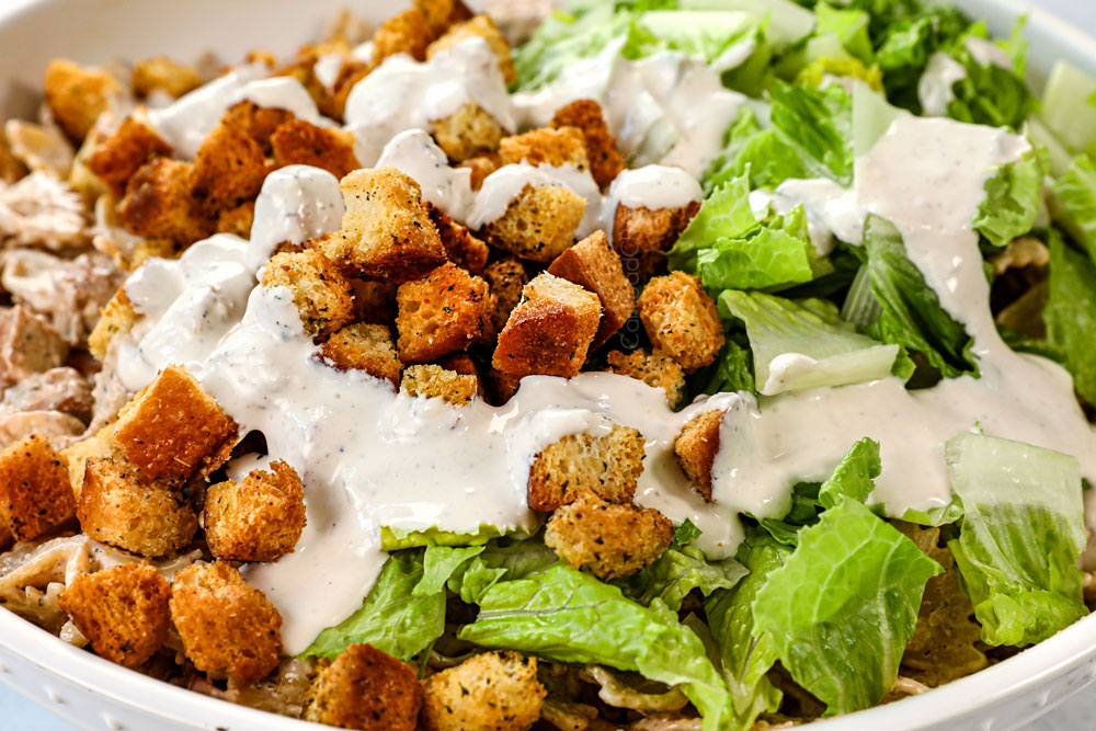 showing how to make Chicken Caesar Pasta Salad by adding the Romaine lettuce and the rest of the Caesar Dressing to the salad