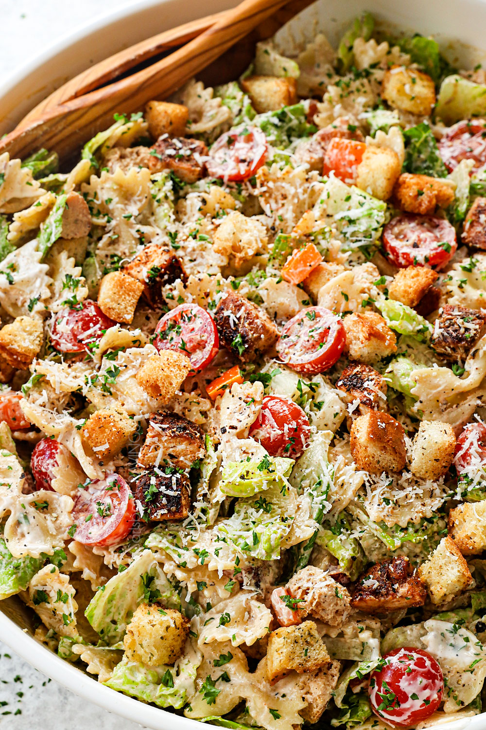 up close of serving Chicken Caesar Pasta Salad in a white bowl with freshly grated Parmesan cheese